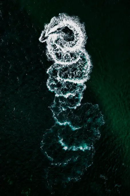 Luftaufnahme einer Gischtspur auf dunklem Wasser, dekoratives Element im Bereich zu Preisen und Transparenz.